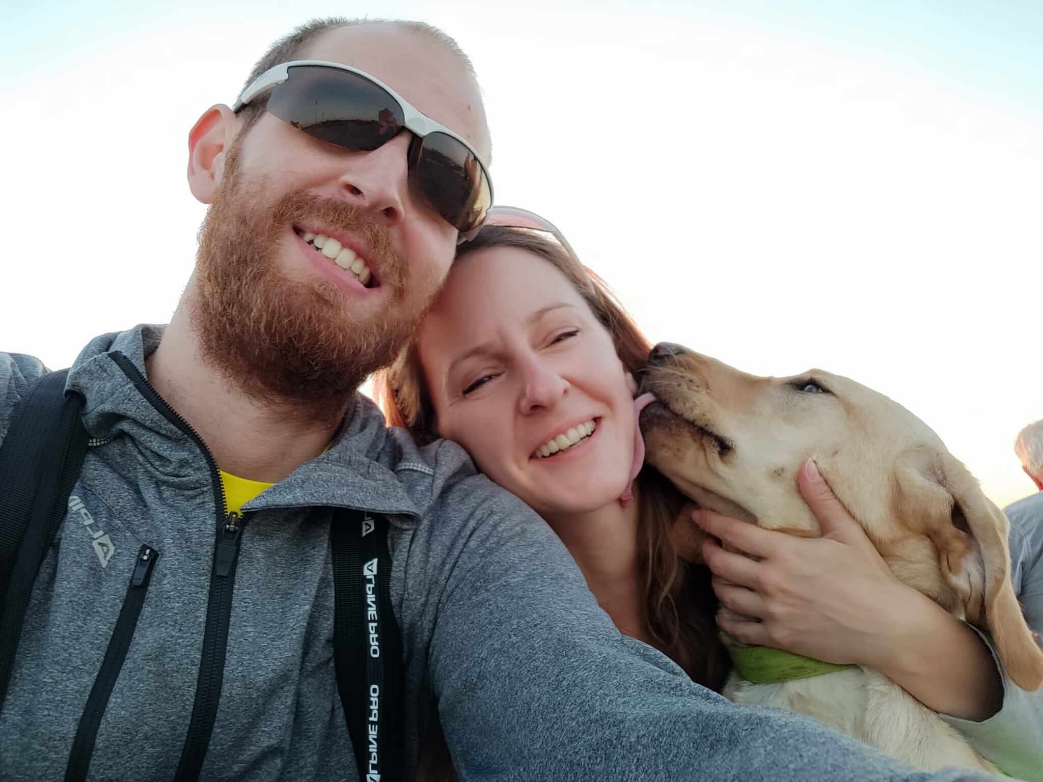 Selfie fotografia na ktorej je vychovávateľka so svojim partnerom a žltá labradorka. Obaja sa schuti smejú a labradorka oblizuje svojej vychovávateľke líce.